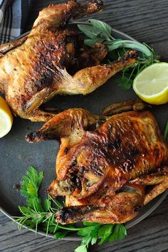 two whole chicken on a plate with lemons and parsley next to it,