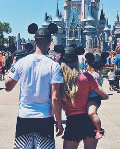 a man and woman standing in front of a castle with mickey mouse ears on their heads