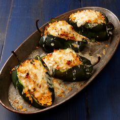 some green peppers with cheese on them sitting in a metal pan next to a blue wooden table