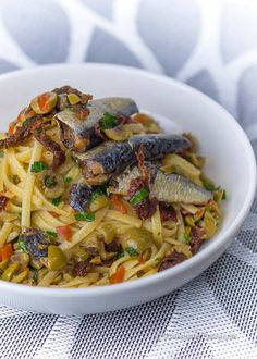 a white bowl filled with pasta and fish on top of a table next to a napkin