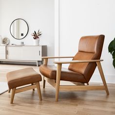 a living room with a chair, ottoman and mirror on the wall next to a potted plant