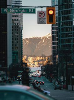 a traffic light hanging over a street next to tall buildings with snow covered mountains in the background