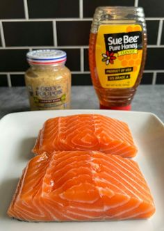 two raw salmon fillets on a white plate next to mustard and seasoning bottles