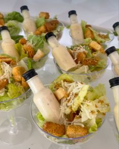 several glasses filled with salad and dressing sitting on a white tablecloth covered table top