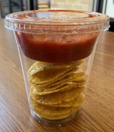 a plastic container filled with tortilla chips and ketchup sitting on top of a wooden table