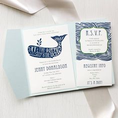 two wedding cards on top of each other next to a white ribbon and some silverware