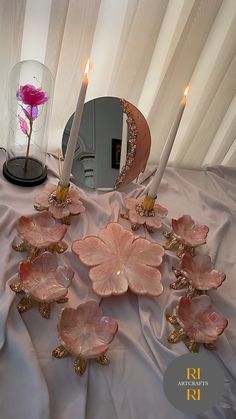 some pink flowers and candles on a white table cloth with a mirror in the background