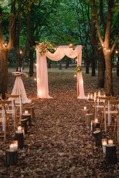 an outdoor wedding set up in the woods with candles and drapes on the ground