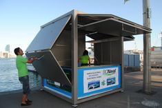 a man standing next to a small booth near the water with people looking at it