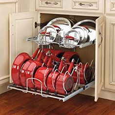 an open dish rack with red pots and pans on it in a white kitchen