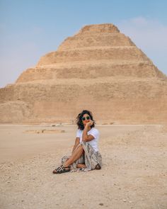 a woman sitting on the ground in front of a large pyramid with her hand to her face