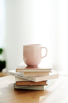 a stack of books with a pink coffee cup on top