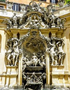 an ornate fountain in front of a building with statues on the sides and above it