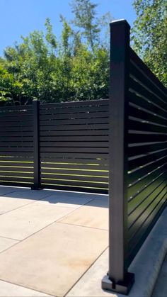 a black metal fence on the side of a sidewalk with trees in the back ground