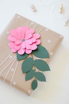 a gift wrapped in brown paper with pink flower on top and green leaves attached to it