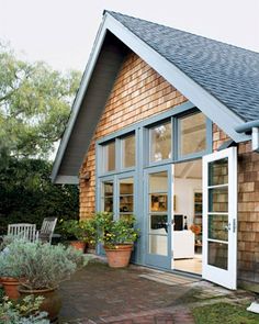 a wooden house with glass doors and windows on the front door is surrounded by potted plants