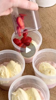 someone is adding strawberries to some ice cream in plastic containers on a wooden table