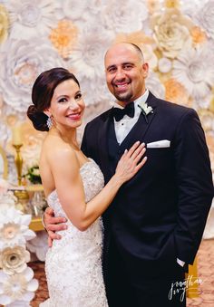 a bride and groom standing next to each other in front of a floral backdrop at their wedding