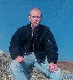 a man sitting on top of a large rock next to a field and blue sky