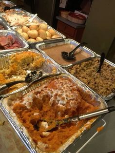 many trays of food are lined up on a table with utensils in them