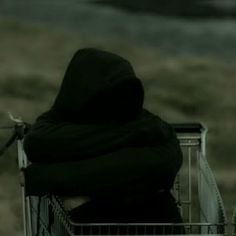 a person sitting in a shopping cart with their back turned to the camera and looking down