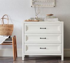 a white dresser sitting next to a basket on top of a wooden chair in front of a wall