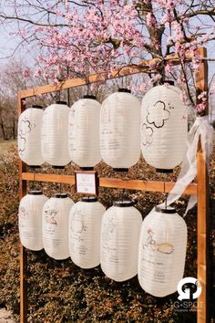 white paper lanterns are hanging from a wooden rack in front of pink flowers and trees