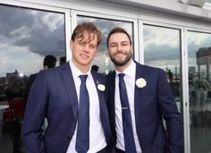 two men in suits standing next to each other near glass doors and looking at the camera