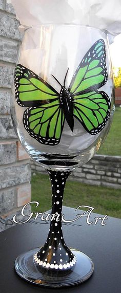 a wine glass with a butterfly painted on the side sitting on top of a table