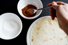 a person is spooning something out of a bowl next to a tortilla