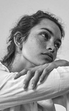 a black and white photo of a woman with freckled hair leaning on a chair