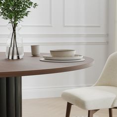 a dining room table with two plates and a vase on it, next to a plant