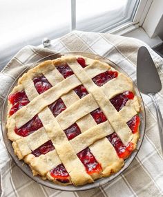 a pie sitting on top of a table next to a fork and knife with a window in the background