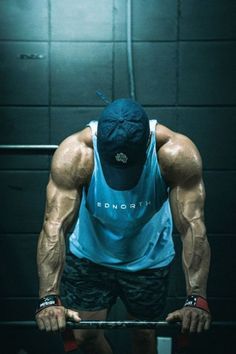 a man is doing squats on a bar in the gym while wearing a blue tank top