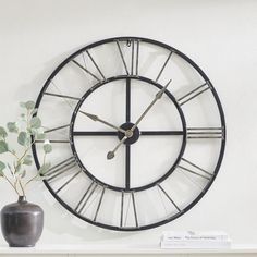 a clock on the wall next to a vase with a plant in it and some books