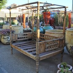 a wooden bed frame sitting next to potted plants and other plant pots on the ground