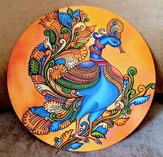 a colorful peacock painted on an orange plate sitting on a couch next to a pillow