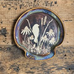 a bird sitting on top of a plate with wildflowers in the center and grass growing out of it