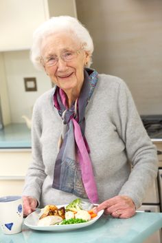 an older woman sitting at a table with a plate of food