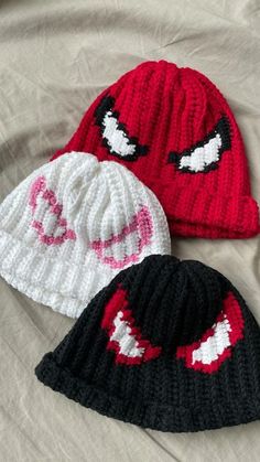 three knitted beanies with different designs on them sitting on top of a bed