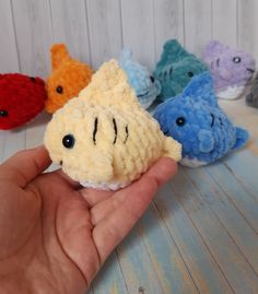 a hand holding a small crocheted fish in front of five other stuffed animals