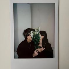 a couple kissing each other with flowers in front of their face on a white wall