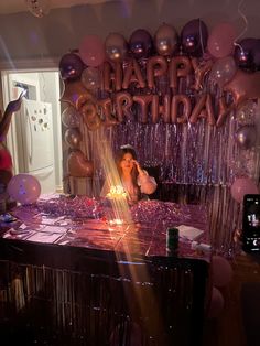 a woman sitting in front of a birthday cake with candles on it and balloons all around her