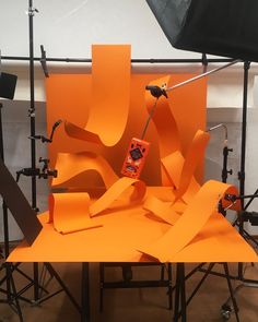 an orange sculpture sitting on top of a tripod in front of a black backdrop