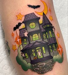 a halloween themed tattoo with a house and bats on the side of her leg,