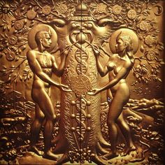 two women standing next to each other in front of a gold wall panel with an intricate design on it