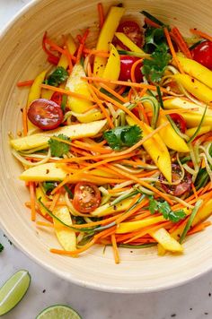 a white bowl filled with vegetables on top of a table next to sliced limes