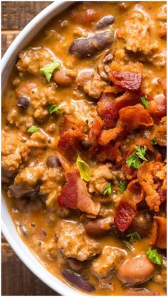 a white bowl filled with beans, bacon and other food on top of a wooden table