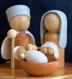 two wooden figurines holding a baby in a bowl on top of a table