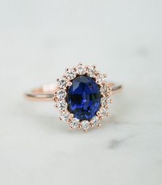 a tan gold ring with an oval blue sapphire surrounded by small white diamonds